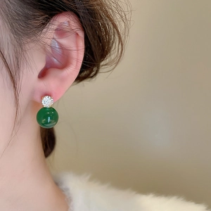 Detail of elegant earrings with deep green round beads and sparkling zircon on a model