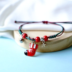 Detail of handmade braided Christmas bracelet with Santa sock charm and bell on wooden stand