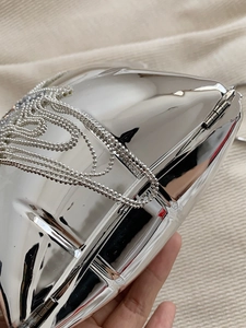 Detail showing polished silver heart-shaped clutch bag with long metallic fringe tassels