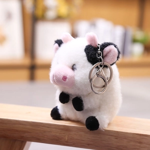 Llavero de vaca de peluche en blanco y negro con detalles rosas sobre fondo de madera