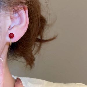 Macro detail of elegant red pearl clip-on earring worn on model's earlobe with gold metal