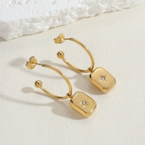 Macro detail of gold-plated stainless steel hoop earrings with starburst pendant and zircon