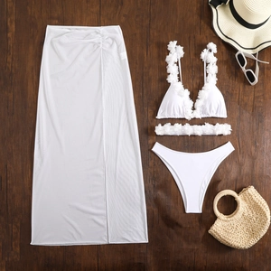 Flat lay of white bikini with 3D floral appliqués and mesh skirt on wood background