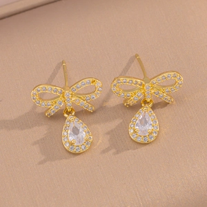 Macro view of gold bowknot teardrop earrings with white zircon on beige texture