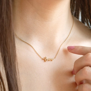Close-up of a 18K gold stainless steel necklace with a cursive love pendant on model
