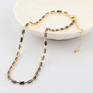 Collier ras du cou doré avec zircons noirs rectangulaires présenté dans un plat en céramique