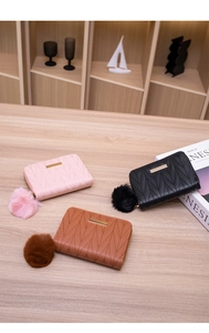 Three quilted short wallets in pink, black, and tan colors with fluffy pompom keychains