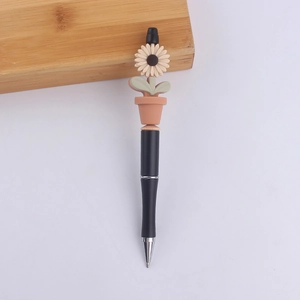 Detailed view of sunflower plant charm atop a sleek black plastic ballpoint pen