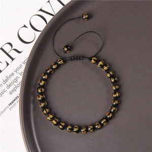 Macro detail of hand-woven bracelet with 6mm black beads and gold mantra symbols