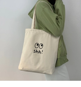 Detalle del bolso tote de lona blanco roto con estampado oo shh llevado por una modelo