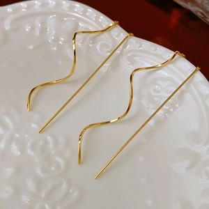 Détail des boucles d'oreilles fils dorés à vagues sur porcelaine blanche élégante