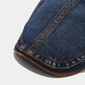 Detail der dunkelblauen Denim-Baskenmütze mit orangefarbenen Nähten und brauner Lederpaspel
