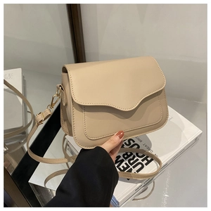 Close-up of beige crossbody bag with wavy flap design and gold hardware detail