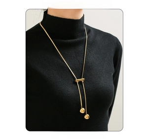 Detail of 18K gold plated long tassel sweater necklace with twin bead charms on black fabric