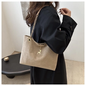 Beige Wildleder-Einkaufstasche mit Goldkette und Hirsch-Anhänger an der Schulter des Models
