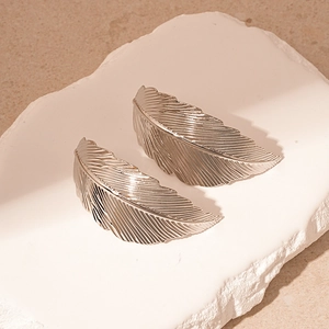 Close-up of silver metal leaf earrings with detailed feather texture on a stone base