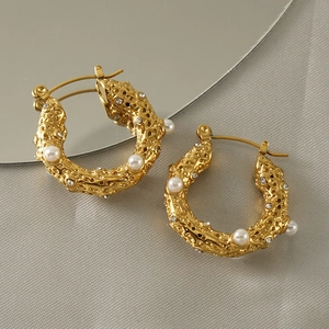Détail de boucles d'oreilles dorées 18k à texture lave avec perles et cristaux sur miroir