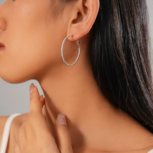 Detail shot of a silver twisted hoop earring on a model featuring metallic texture