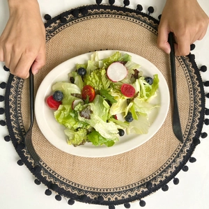 Minimalist round woven jute placemat with black pompom tassels and geometric border