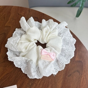 Détail de chouchou en dentelle blanche avec petit nœud rose sur bois sombre