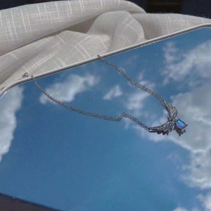 Silver angel wings necklace with blue teardrop moonstone pendant on a sky background