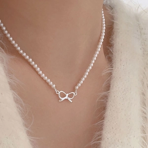 Close-up of a silver bow necklace with small white faux pearls worn over a white fur coat