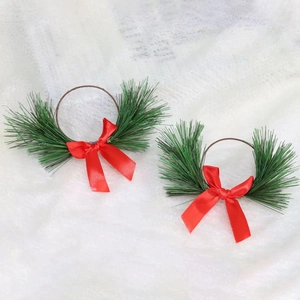 Detail showing two Christmas napkin rings with pine needles and red satin bows on fabric