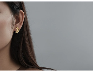 Close-up of minimalist gold flower studs on ear showing three stacked matte petals