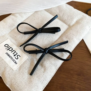 Close-up of black faux leather bow hair clips on a canvas bag and wooden background