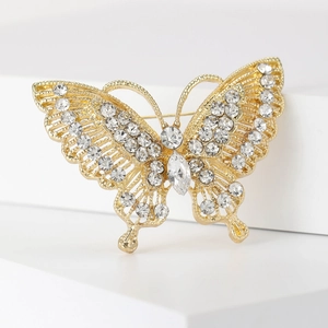 Retro butterfly brooch with gold plating and sparkling rhinestones on white pedestal