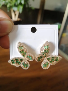 Macro shot of gold butterfly earrings with emerald gemstones and micro zircon stones