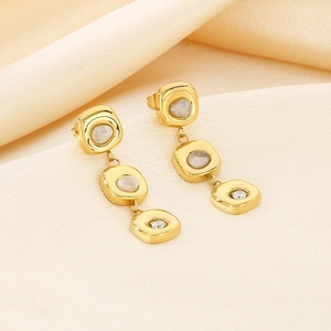 Detailed view of gold square drop earrings with cat eye stones on cream fabric