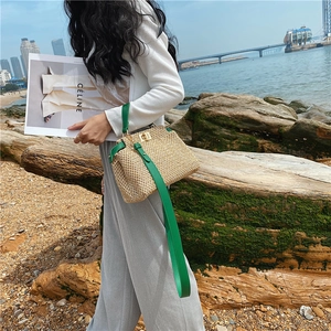 Detail of hand-woven straw bag featuring bright green leather handles and gold swivel lock
