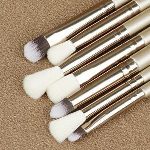 Détail de pinceaux à maquillage dorés avec poils synthétiques sur un tissu marron texturé