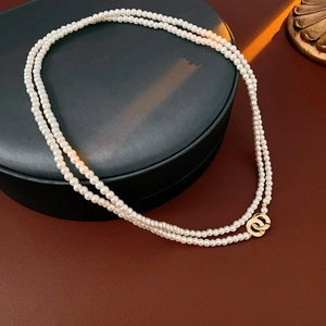Close-up of double-layer pearl necklace with golden interlocking rings on a leather surface