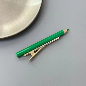 Détail de la pince à cheveux crayon vert créative avec pince crocodile dorée sur fond gris