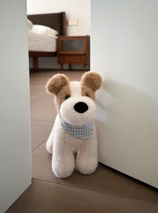 Close-up of cute plush puppy toy with blue checkered bib in a cozy home setting