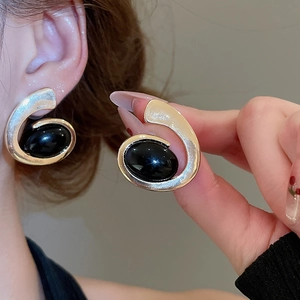 Close-up of golden spiral earrings featuring oval black resin stones on a model