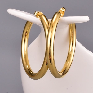 Close-up of large polished gold hoop earrings hanging on a white ceramic display stand