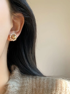 Close-up of a vintage golden pearl stud earring with sparkling zircon halo on model ear