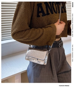 Close-up of silver crocodile texture chain bag worn by model over a brown sweater