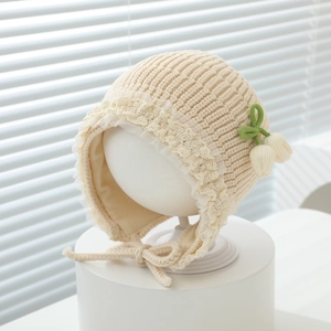 Detail of baby knit bonnet with delicate lace trim and green knitted flower accents