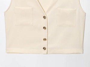 Détail du gilet sans manches crème avec quatre boutons dorés gaufrés et deux poches plaquées