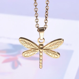 Macro shot of gold dragonfly pendant with detailed metallic texture and delicate chain