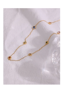 Close-up of gold titanium steel necklace with multi-colored gemstones on white linen