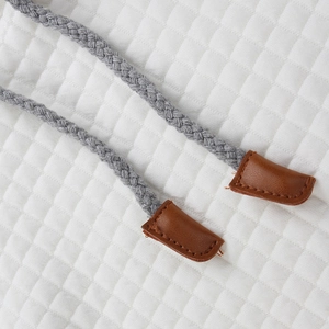 Close-up of braided gray drawstrings with brown leather tips on white quilted fabric