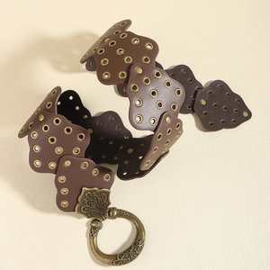 Dettaglio cintura in pelle marrone con borchie vintage e fibbia metallica incisa
