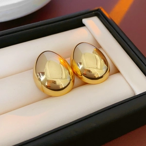 Gros plan de boucles d'oreilles dorées en forme d'œuf dans un écrin à bijoux noir