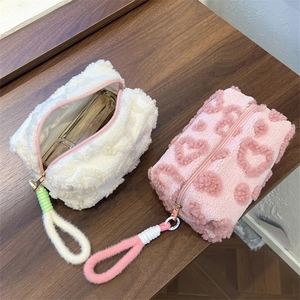 Detail of plush cream and pink makeup bags with heart patterns and woven handles