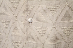 Close-up of beige jacquard shirt fabric with geometric pattern and white button detail